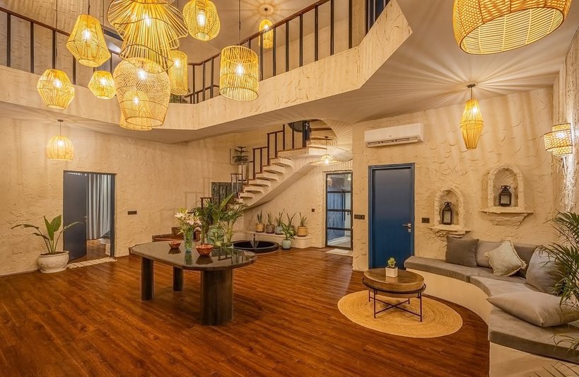 Double-height living area with woven pendant lights and an indoor water feature in a villa in Gurgaon